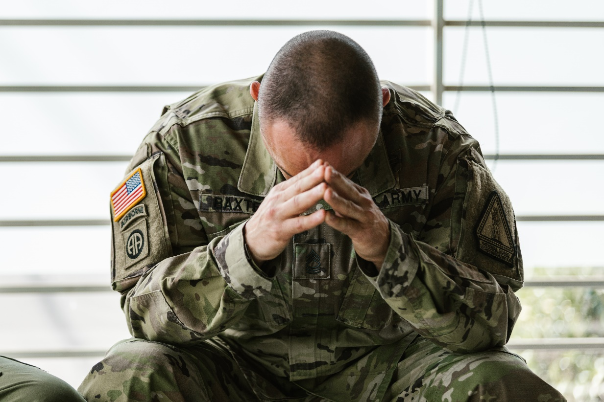 A soldier sitting with their head bowed down, looking distressed.