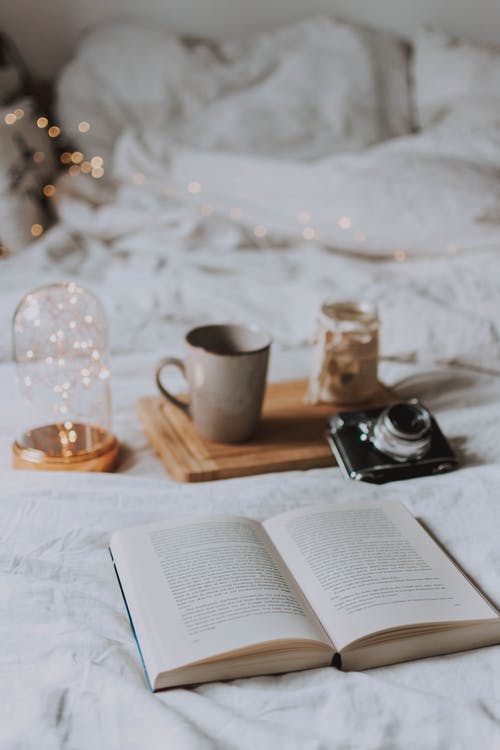 A book displayed aesthetically next to a mug, camera, and fairy lights